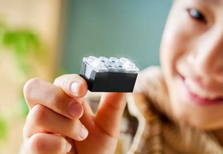 A child holding a LEGO SMART Brick with LED lights glowing through the transparent top